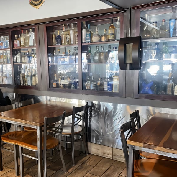 Interior of La Penca Azul, featuring a tequila display cabinet above wooden tables and chairs.