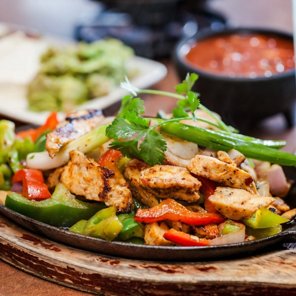 Sizzling chicken fajitas with bell peppers and onions, garnished with cilantro, served with salsa and guacamole.