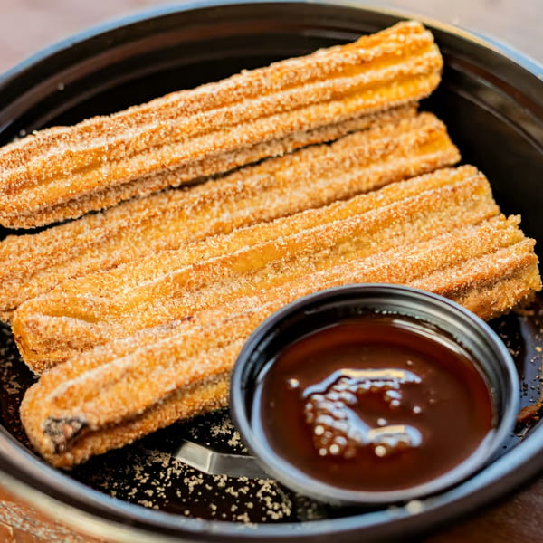 Four golden churros coated in sugar and cinnamon, with a side of chocolate dipping sauce.