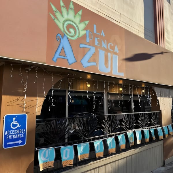 Exterior of La Penca Azul restaurant with a blue accessible entrance sign and decorative banners.