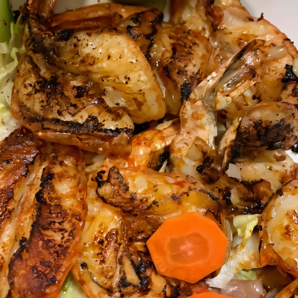 Close-up of grilled shrimp with charred marks, served with lettuce and a carrot slice.