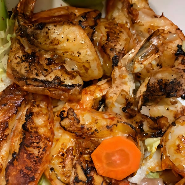 Close-up of grilled shrimp with a dark glaze, served with shredded lettuce and a carrot slice.