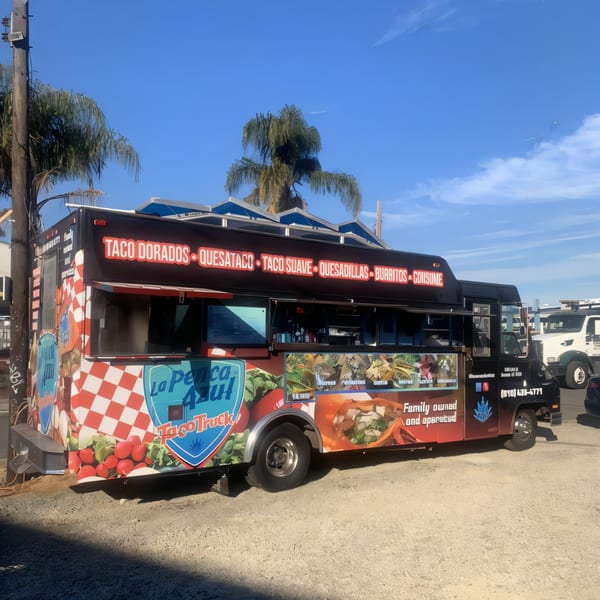 La Penca Azul Taco Truck, a black food truck with a vibrant checkered and food-themed wrap.