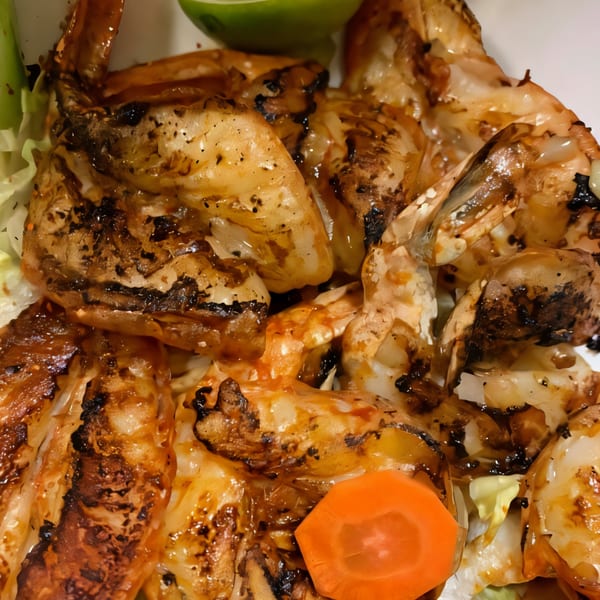 Close-up of grilled shrimp with charred edges, served with a slice of carrot and lime.