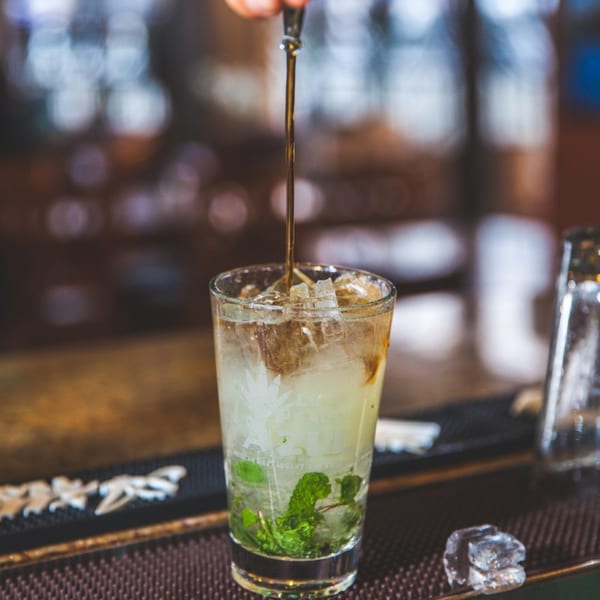 A bartender pouring a dark liquid into a mojito with ice and mint at La Penca Azul.