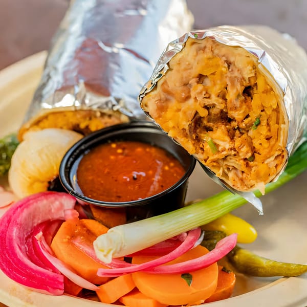 Two foil-wrapped burritos, salsa, pickled onions, carrots, and green onions on a plate.