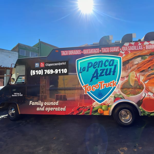 La Penca Azul Taco Truck, a black food truck with vibrant Mexican food graphics under a sunny sky.