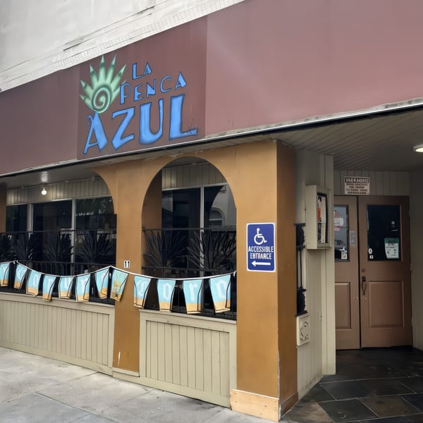 Exterior of La Penca Azul restaurant with a brown facade, arched windows, and a blue accessible entrance sign.