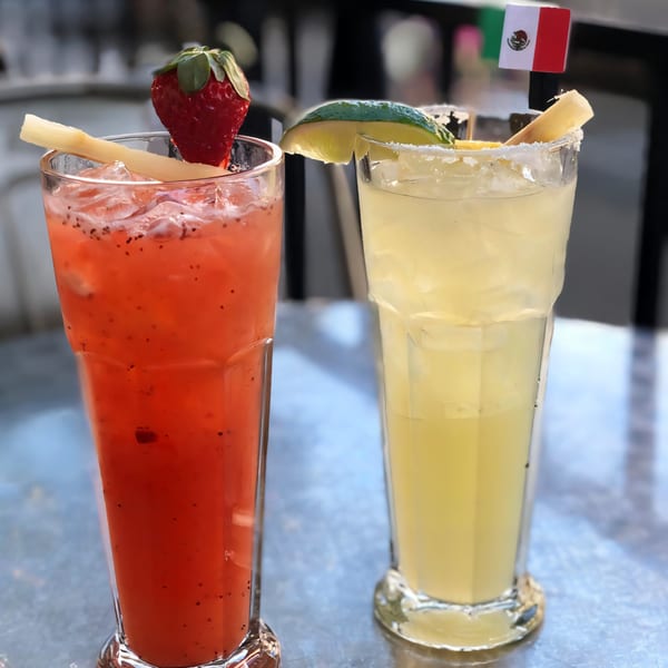 Two La Penca Azul drinks, a red strawberry cocktail and a yellow margarita, on a table.