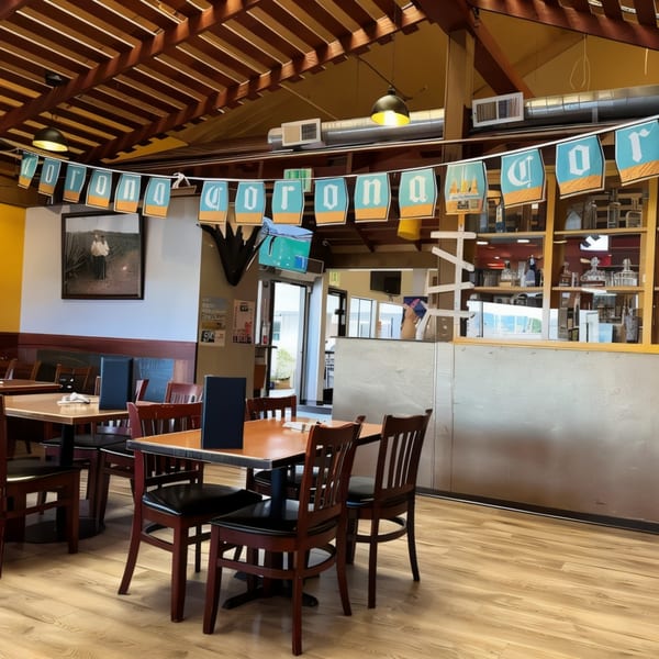 Interior of La Penca Azul restaurant with wooden tables and chairs, and a "Corona" banner hanging.