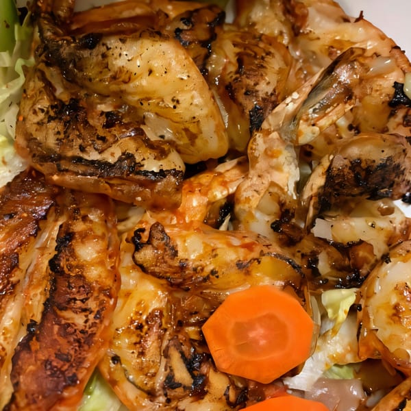 Close-up of grilled shrimp with charred edges, served on a bed of lettuce with carrot slices.