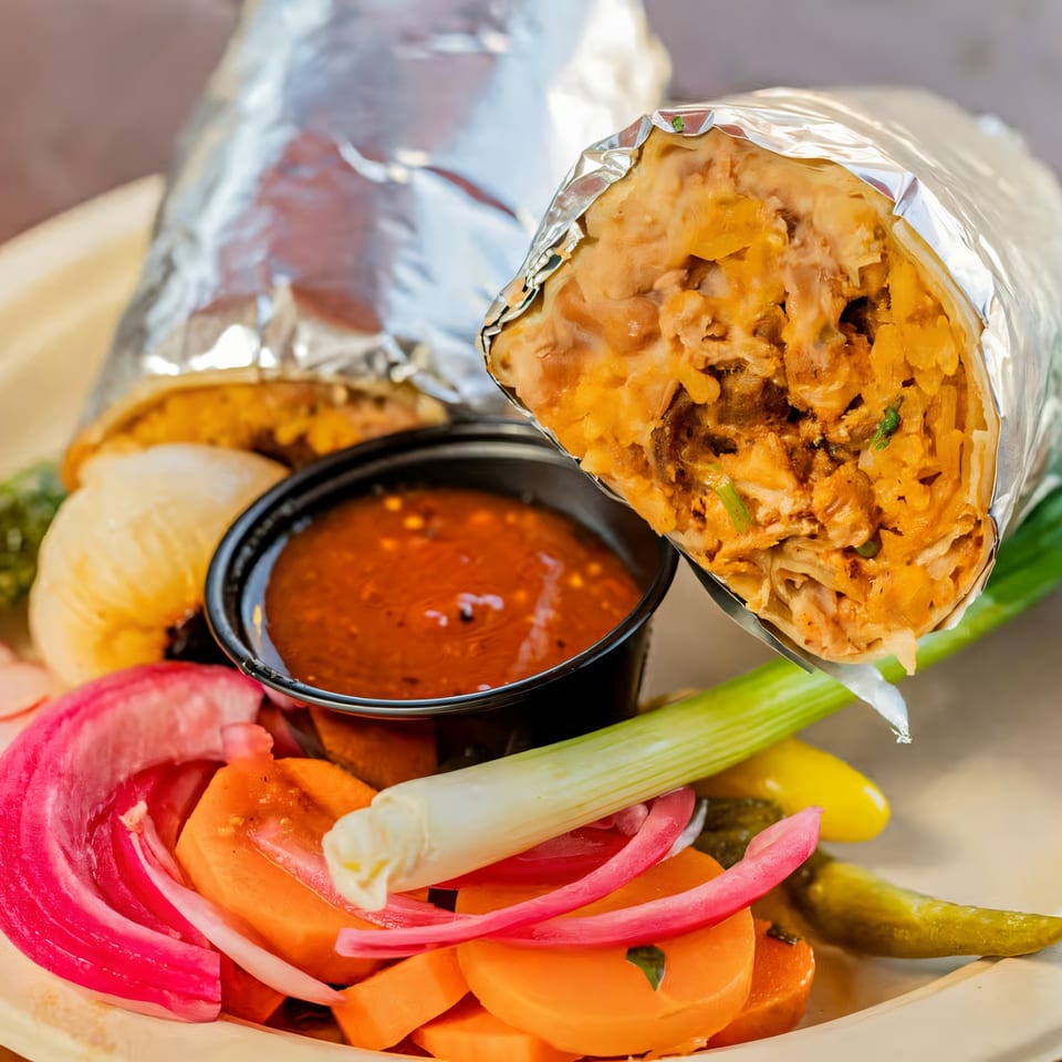 Two foil-wrapped burritos, salsa, pickled onions, carrots, and green onions on a plate.