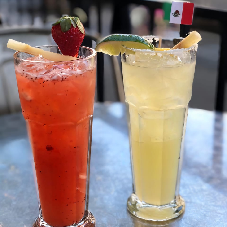 Two La Penca Azul drinks, one red with a strawberry, one yellow with a lime and Mexican flag.